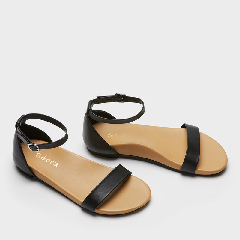  Front view of black leather sandal with a padded heel cup and toe strap. The footbed is nude, and fitted with arch support. 